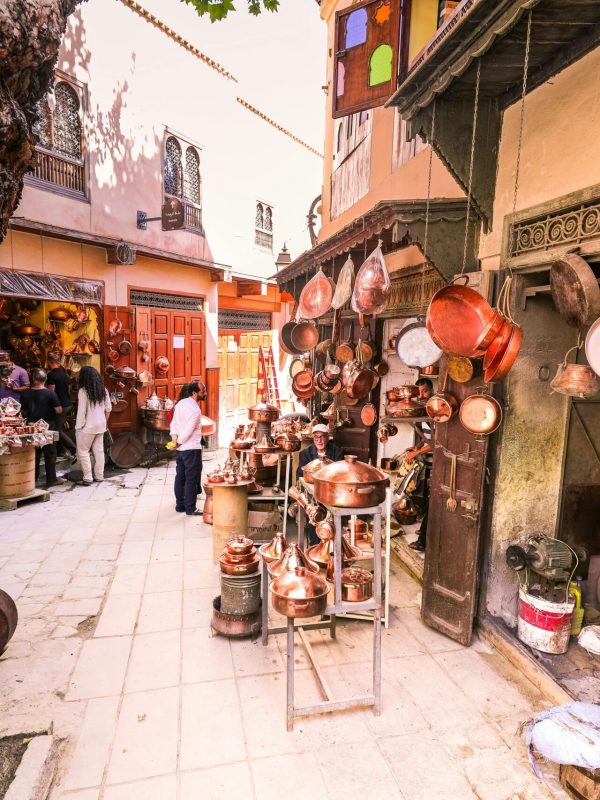 pexels-photo-2610821-2610821 A vibrant outdoor market scene displaying hanging brass pots and people shopping.